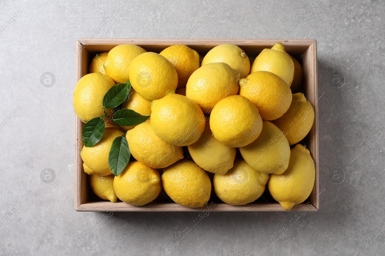 Photo of Fresh lemons in wooden crate on grey table, top view