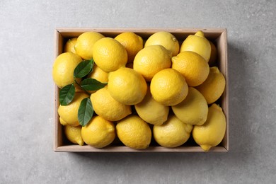 Fresh lemons in wooden crate on grey table, top view