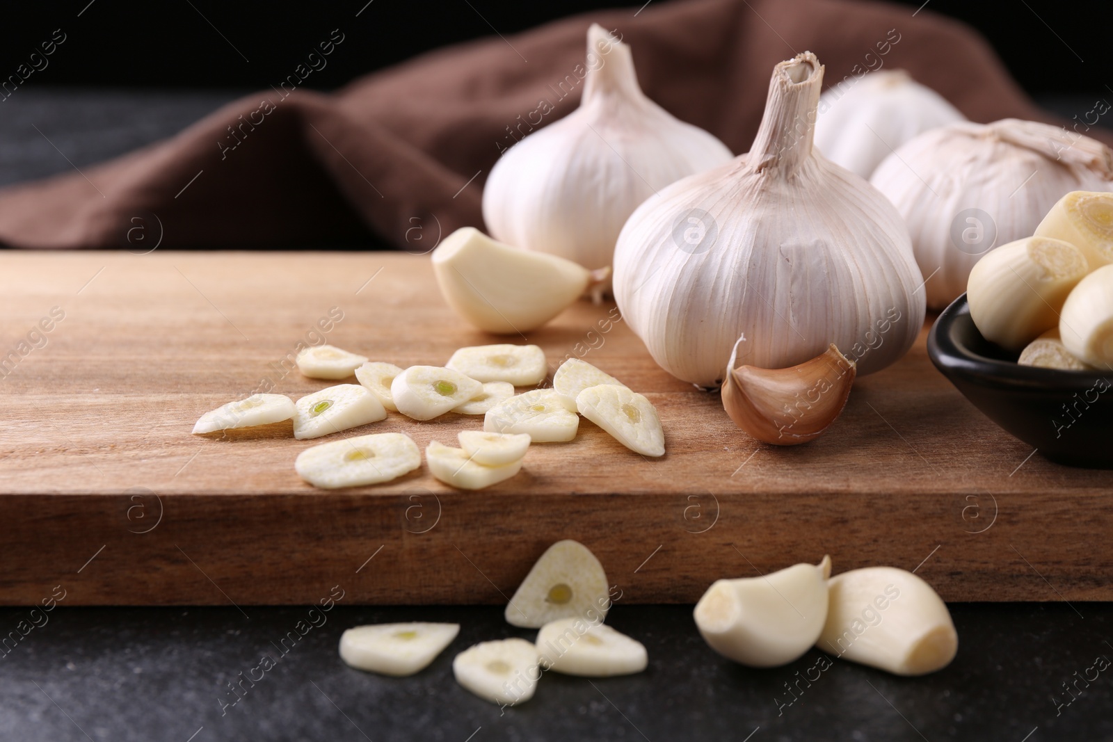 Photo of Aromatic cut garlic, cloves and bulbs on dark table, closeup