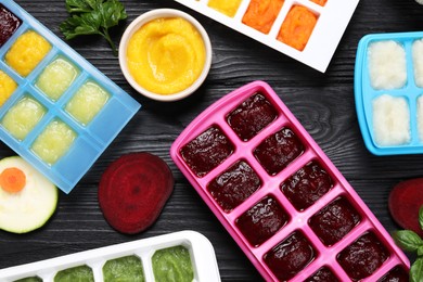 Photo of Different frozen purees in ice cube trays and ingredientsblack wooden table, flat lay. Ready for freezing