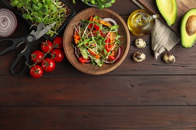 Salad with fresh organic microgreen in bowl on wooden table, flat lay. Space for text