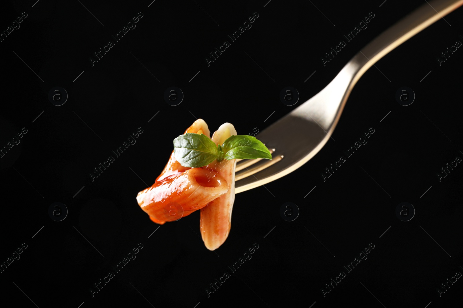 Photo of Delicious penne pasta with tomato sauce on fork against  black background