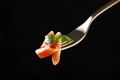 Delicious penne pasta with tomato sauce on fork against  black background