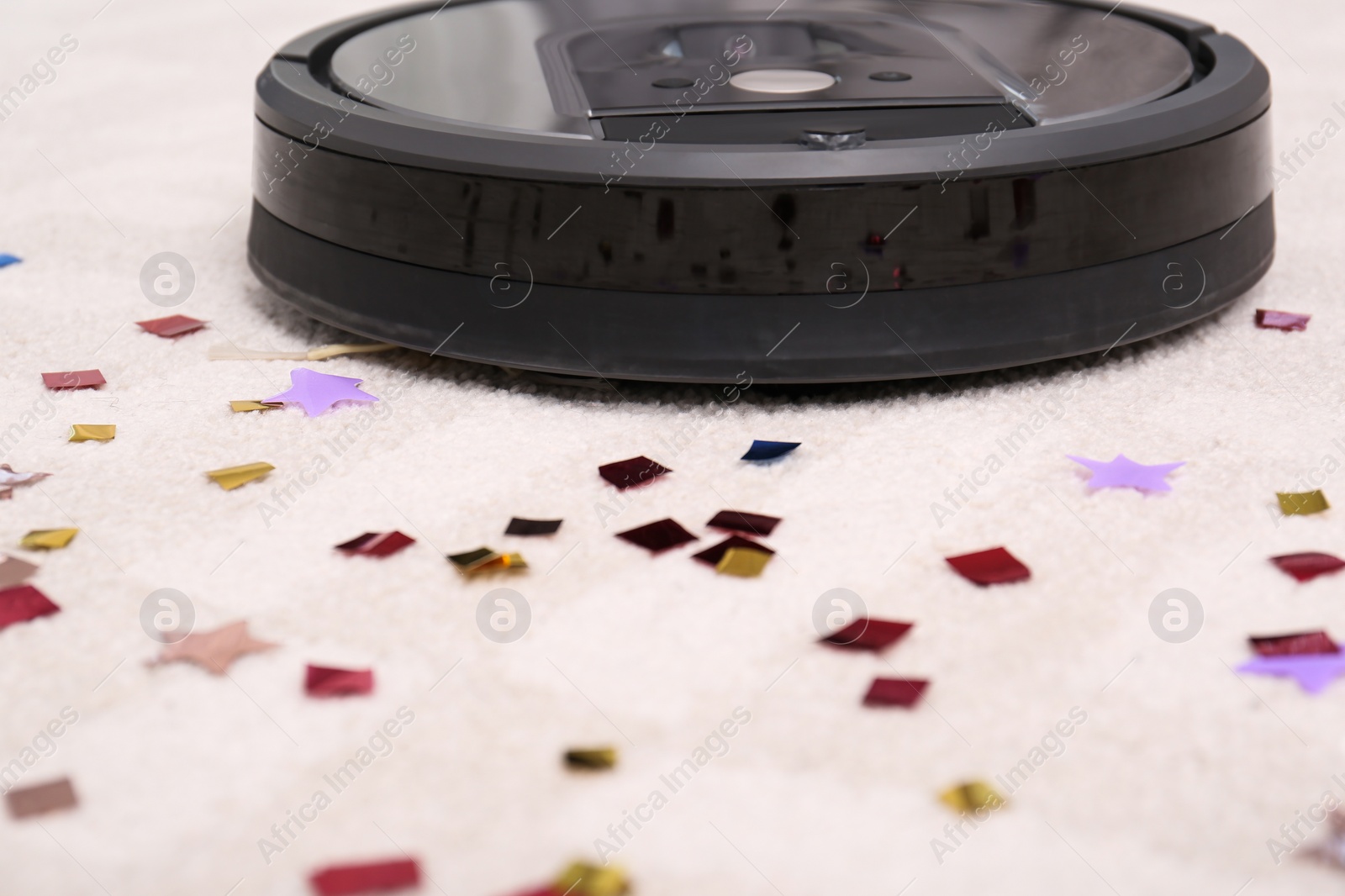 Photo of Modern robotic vacuum cleaner removing confetti from carpet, closeup. Space for text