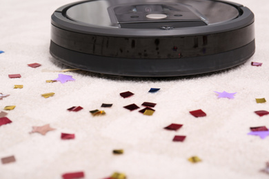 Modern robotic vacuum cleaner removing confetti from carpet, closeup. Space for text