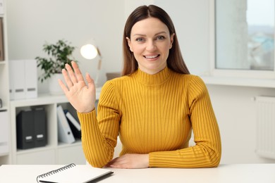 Woman waving hello during video chat at table in office, view from web camera