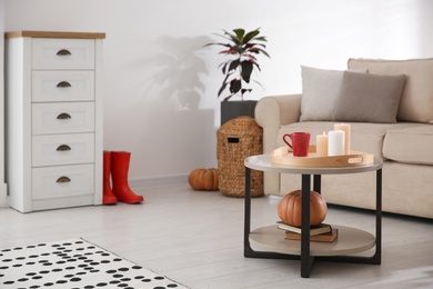 Photo of Burning candles and cup of drink on table indoors. Cozy living room interior inspired by autumn colors