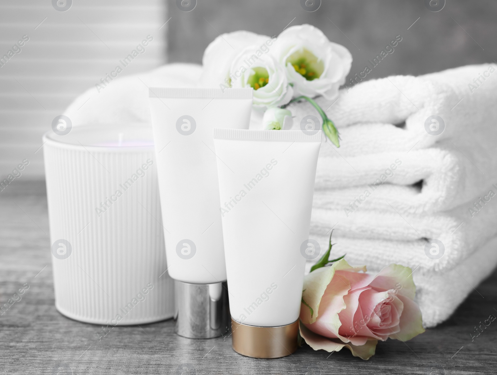 Photo of Cosmetic products, scented candle and folded towels with flowers on wooden table indoors