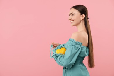 Photo of Woman with string bag of fresh lemons on pink background, space for text