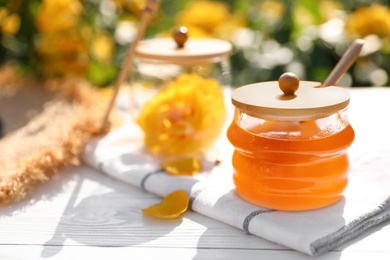 Photo of Jar with fresh rose honey on white wooden table outdoors. Space for text