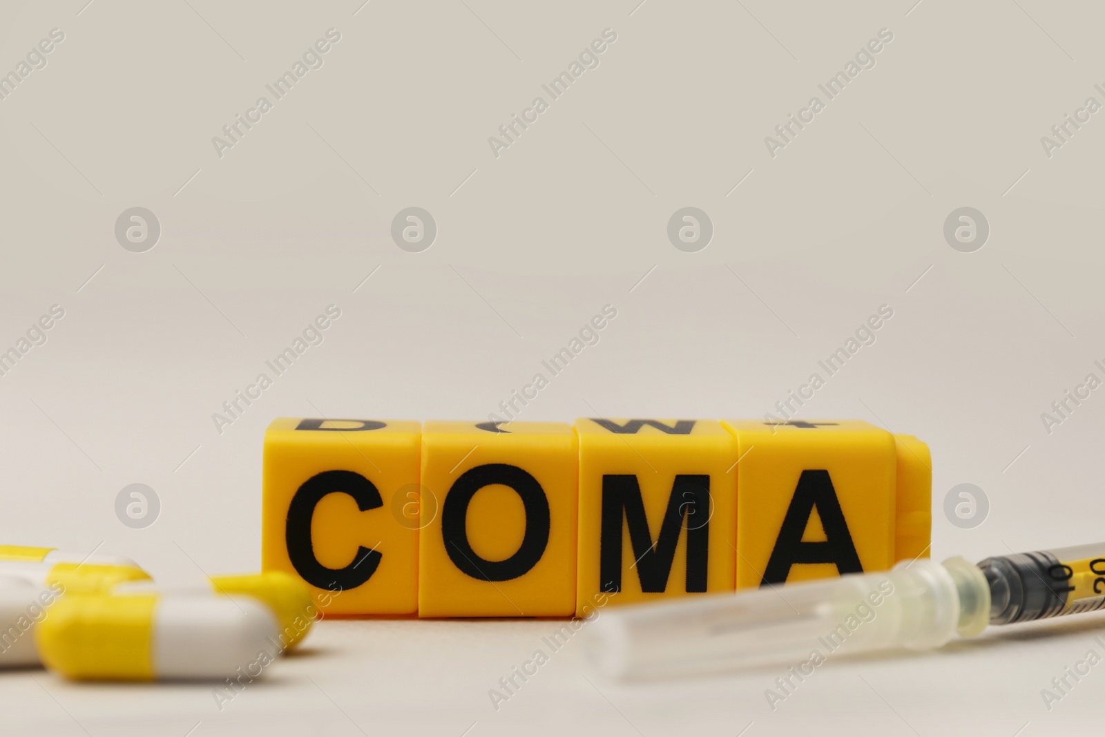 Photo of Word Coma of cubes, syringe and pills on beige background, closeup