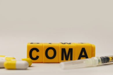Photo of Word Coma of cubes, syringe and pills on beige background, closeup