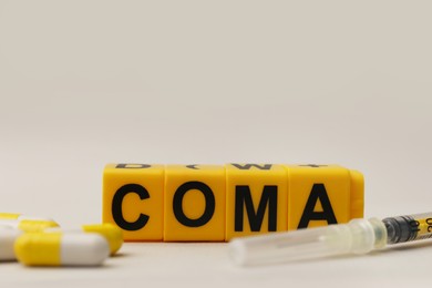 Word Coma of cubes, syringe and pills on beige background, closeup