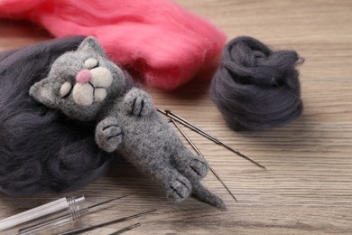 Photo of Felted cat, wool and tools on wooden table, closeup