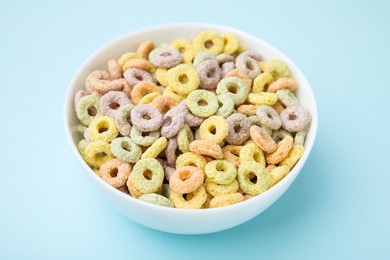 Photo of Tasty cereal rings in bowl on light blue table, closeup