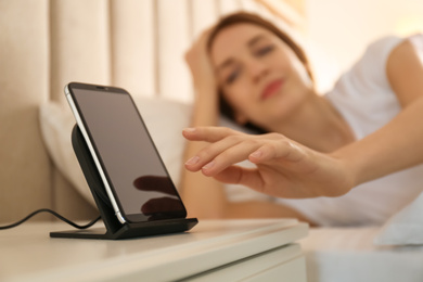 Woman taking smartphone from wireless charger in bedroom