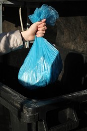 Photo of Woman throwing trash bag full of garbage in bin outdoors, closeup