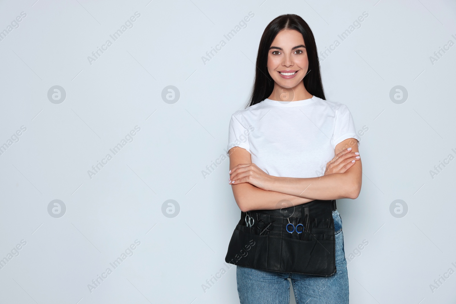 Photo of Portrait of happy hairdresser with professional tools on light background, space for text