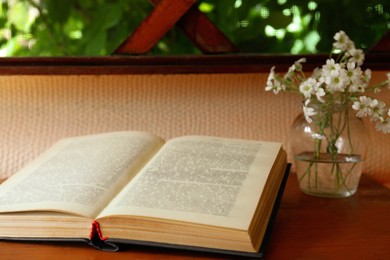 Photo of Open book and beautiful white flowers on wooden table, closeup