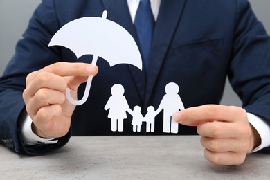 Photo of Man holding cutout paper family and umbrella at table, closeup. Life insurance concept