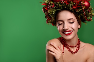Beautiful young woman wearing Christmas wreath on green background. Space for text