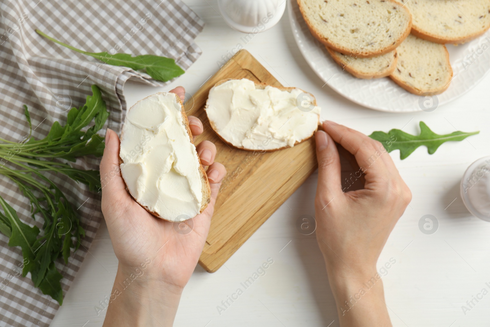 Photo of Woman holding bread with cream cheese at white wooden table, closeup