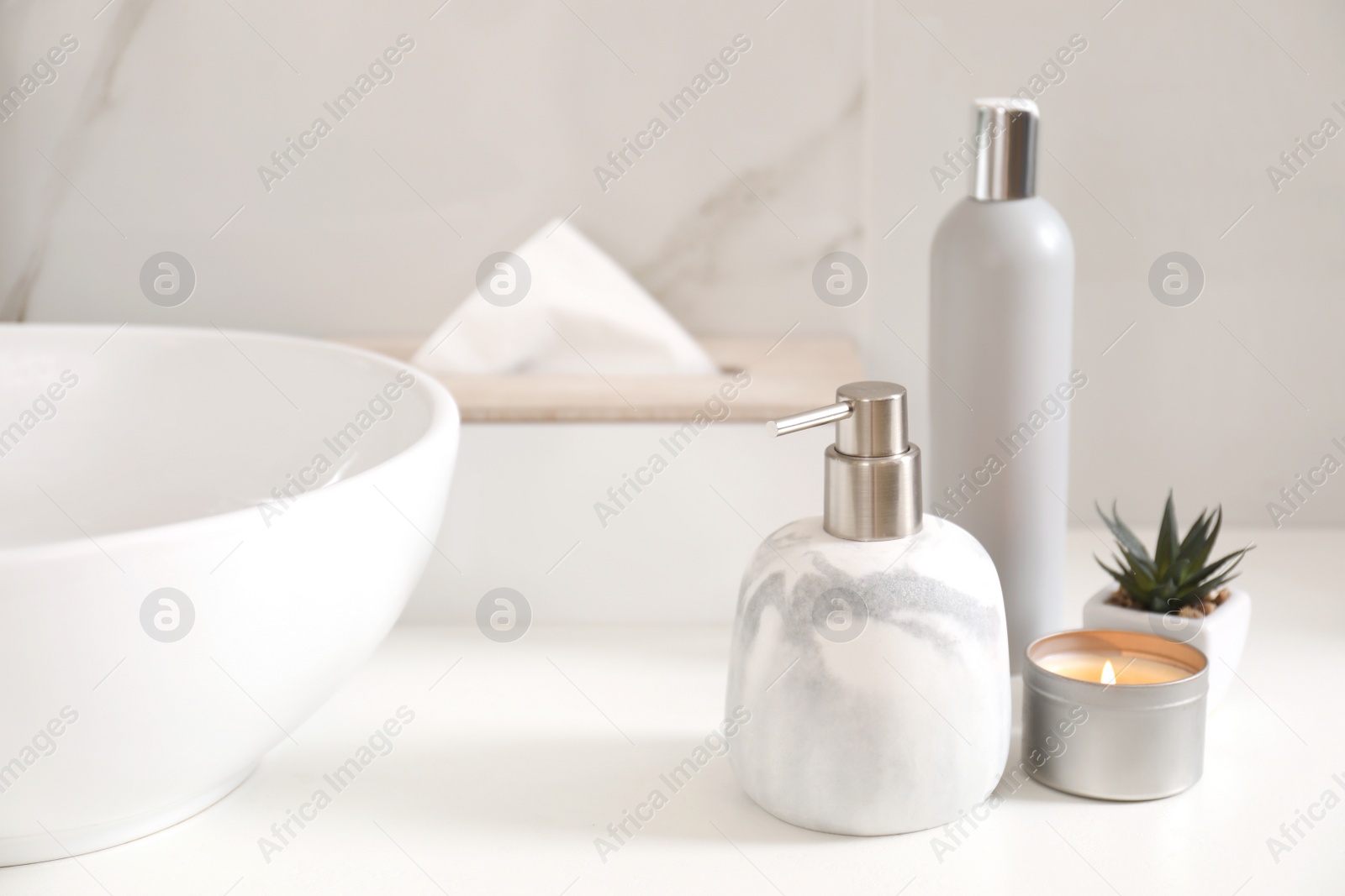 Photo of Toiletries, burning candle and plant near vessel sink in bathroom