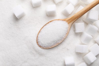 Different types of white sugar and spoon as background, top view