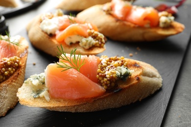 Photo of Tasty bruschettas with salmon and blue cheese on slate plate, closeup