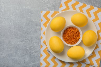 Photo of Yellow Easter eggs painted with natural dye and turmeric powder in bowl on light gray textured table, top view. Space for text