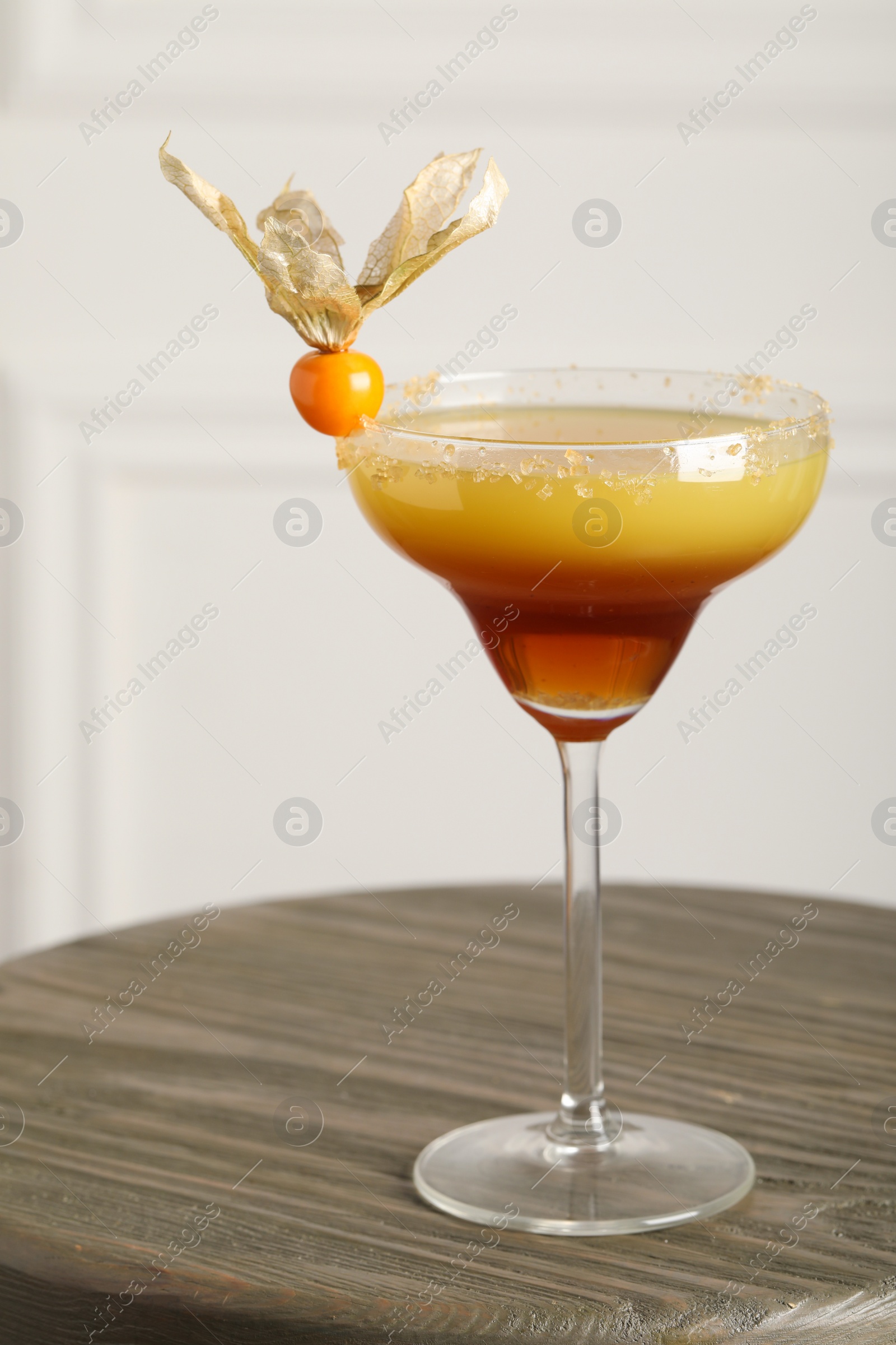 Photo of Refreshing cocktail decorated with physalis fruit on wooden table indoors