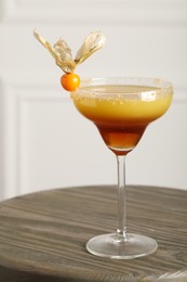 Photo of Refreshing cocktail decorated with physalis fruit on wooden table indoors