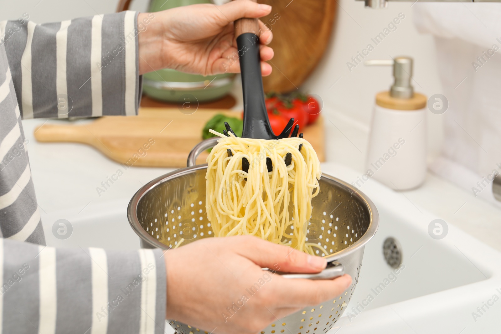 Photo of Woman with colander of cooked spaghetti and pasta server at sink, closeup