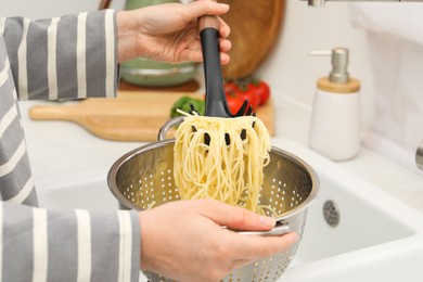 Photo of Woman with colander of cooked spaghetti and pasta server at sink, closeup