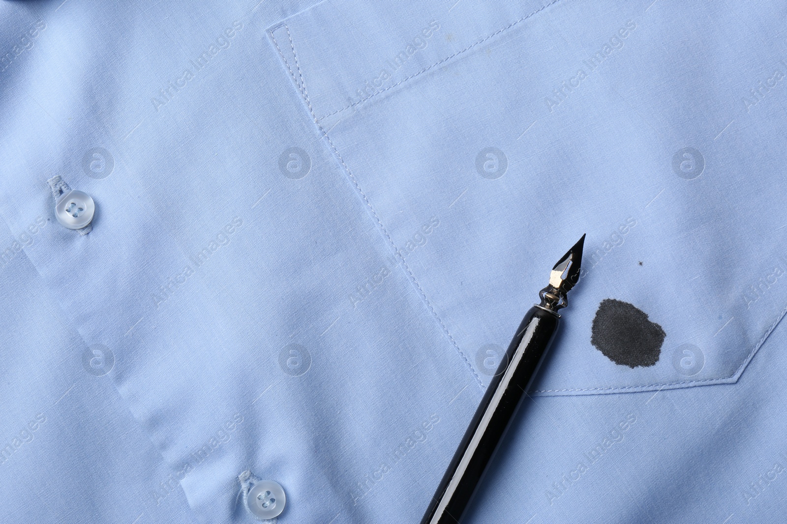 Photo of Black ink stain on light blue shirt and pen, top view. Space for text