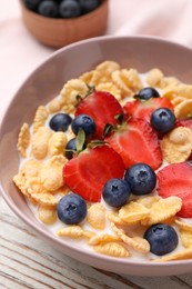 Photo of Bowl of tasty crispy corn flakes with milk and berries on white wooden table, closeup