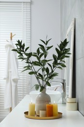 Beautiful plant in vase and burning candles near vessel sink on bathroom vanity