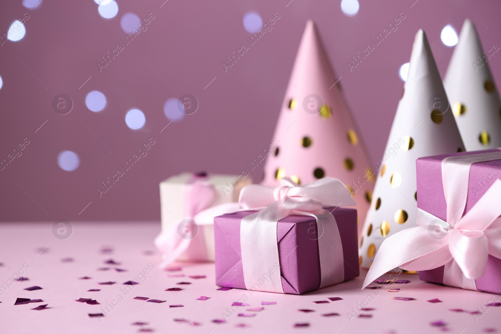 Photo of Gift boxes and party hats on pink table against blurred lights. Space for text