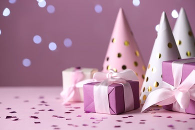Gift boxes and party hats on pink table against blurred lights. Space for text