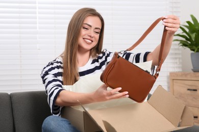 Photo of Happy woman with just unpacked new bag at home. Online store