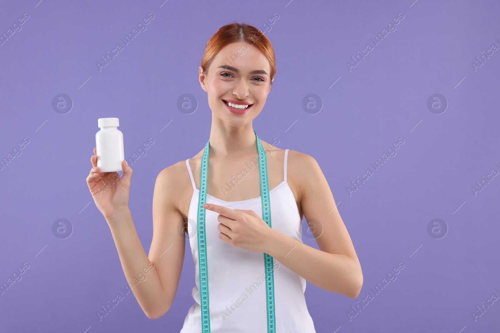Photo of Happy young woman with bottle of pills and measuring tape on purple background. Weight loss