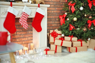 Photo of Beautiful Christmas tree and gifts near decorative fireplace with stockings indoors