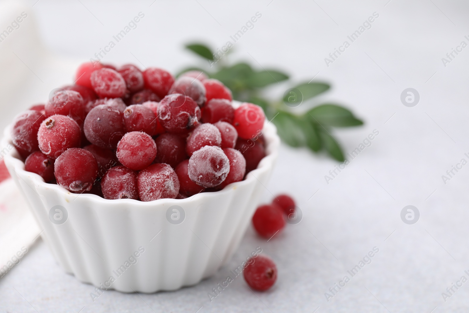 Photo of Frozen red cranberries in bowl on light table, closeup. Space for text