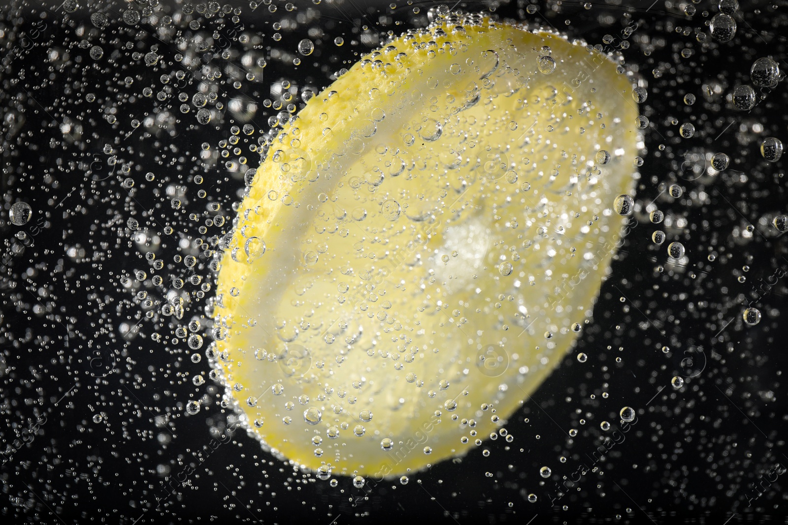 Photo of Juicy lemon slice in soda water against black background, closeup