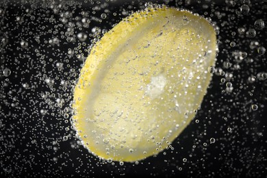 Photo of Juicy lemon slice in soda water against black background, closeup