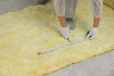 Photo of Worker measuring and cutting insulation material indoors, closeup. Space for text