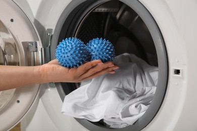 Photo of Woman putting blue dryer balls into washing machine, closeup