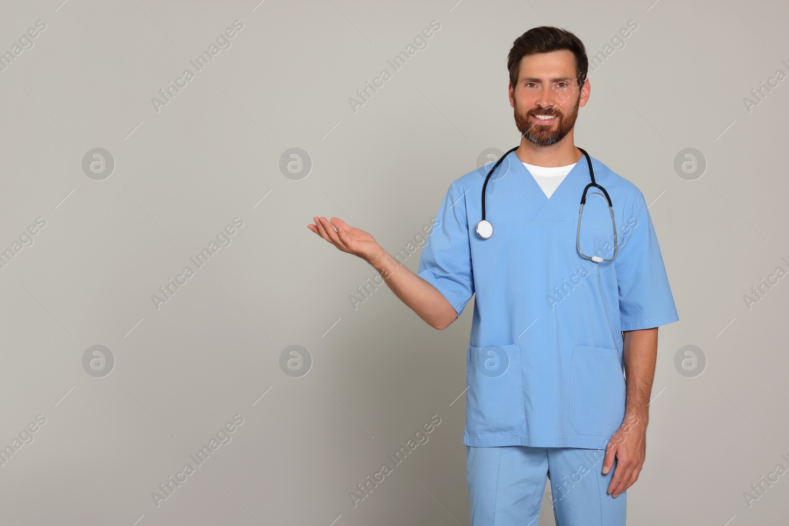 Photo of Happy doctor with stethoscope on light grey background. Space for text