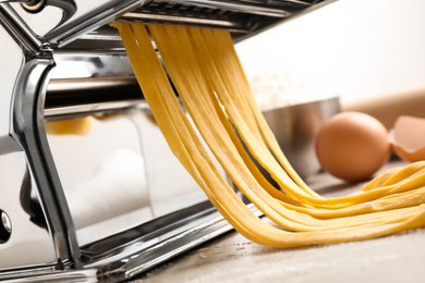 Pasta maker machine with dough on grey table, closeup