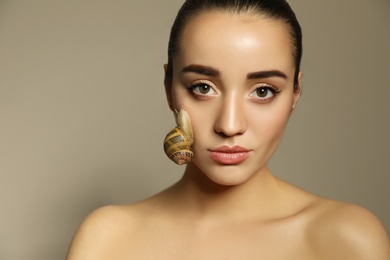 Beautiful young woman with snail on her face against beige background